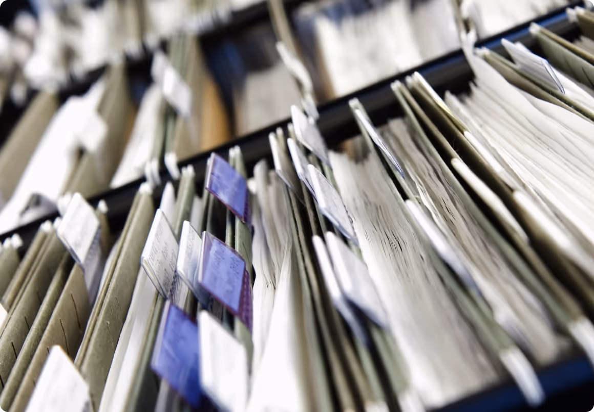 Close-up of rows of filing folders with paper documents, some with blue tabs.